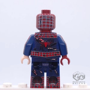 May include: A custom Lego minifigure of Spider-Man, featuring a red and blue costume with a spider emblem on the back. The figure has a red head with a web pattern and is standing on a white base.