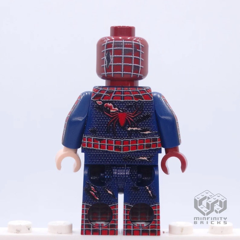 May include: A custom Lego minifigure of Spider-Man, featuring a red and blue costume with a spider emblem on the back. The figure has a red head with a web pattern and is standing on a white base.