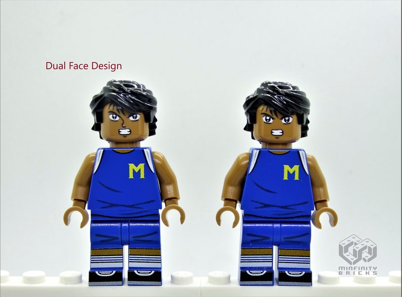 May include: Dual Face Design. A Lego minifigure with black hair, brown skin, and a blue basketball jersey with a yellow "M" on the front. The minifigure has two different facial expressions.