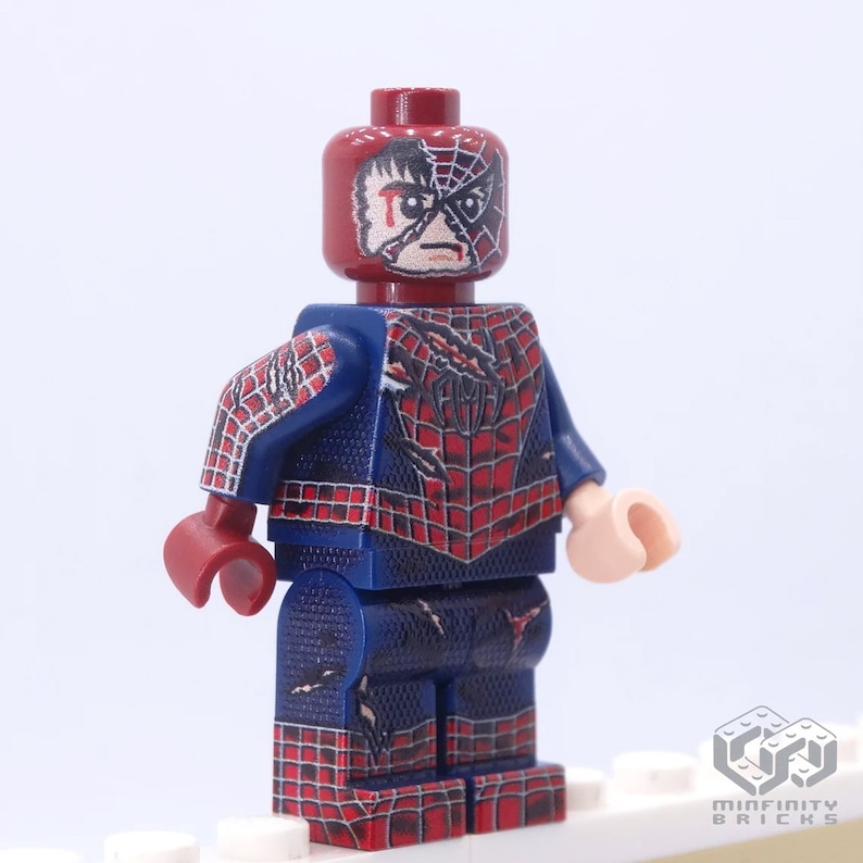 May include: A custom Lego minifigure of Spider-Man in a battle-damaged state. The figure features a red and blue costume with a web design, and a distressed mask revealing a portion of Peter Parker's face. The figure has a light skin tone and red hands.