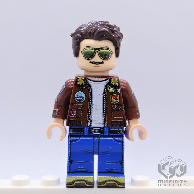 Puede incluir: Una minifigura de Lego que lleva una chaqueta de cuero marr&oacute;n con parches, pantalones vaqueros azules y gafas de sol. La minifigura tiene el pelo casta&ntilde;o y un bigote.