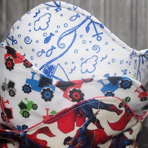 May include: A stack of fabric bowl cozies with different patterns. The top cosy has a white background with blue anchors, fish, and clouds. The middle cosy has tractors in red, blue, and green on a white background. The bottom cosy displays a Superman design.
