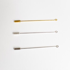 May include: Three metal lapel pins. One is gold-colored, and the other two are silver-colored. Each pin has a straight, thin shaft with a rounded end and a small loop at the opposite end. The pins are displayed against a white background.