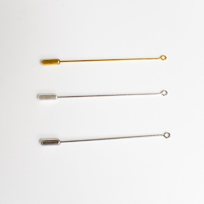 May include: Three metal lapel pins. One is gold-colored, and the other two are silver-colored. Each pin has a straight, thin shaft with a rounded end and a small loop at the opposite end. The pins are displayed against a white background.