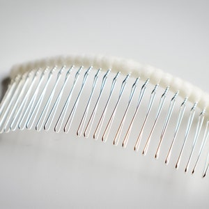 May include: A silver hair comb with a white, fluffy, padded base.