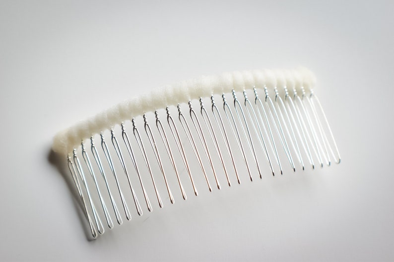 May include: A silver hair comb with a white, fuzzy covering on the top. The comb has a curved shape and is designed for holding hair in place.