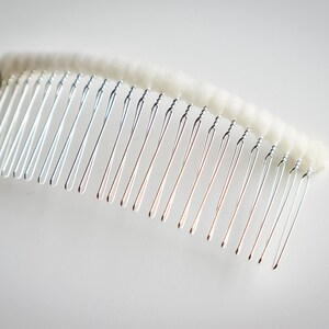 May include: A silver hair comb with a white, fluffy, padded base.