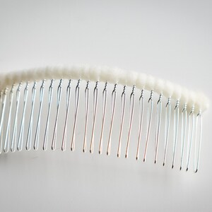 May include: A silver hair comb with a white, fluffy, fabric covering the top.