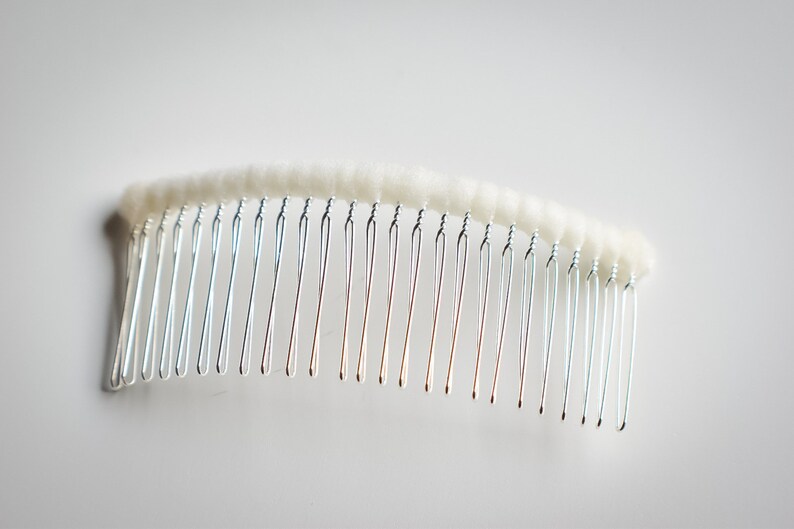 May include: A silver hair comb with a white, fluffy, fabric covering the top.