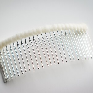 May include: A silver hair comb with white fuzzy padding on the top. The comb has a curved shape and is designed for holding hair in place.