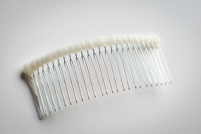 May include: A silver hair comb with white fuzzy padding on the top. The comb has a curved shape and is designed for holding hair in place.
