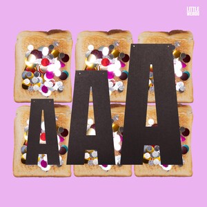 Op de afbeelding: Drie zwarte kartonnen letters die "AAA" spellen, liggen op drie toastjes die bedekt zijn met kleurrijke sprinkles. De toastjes liggen op een roze achtergrond.