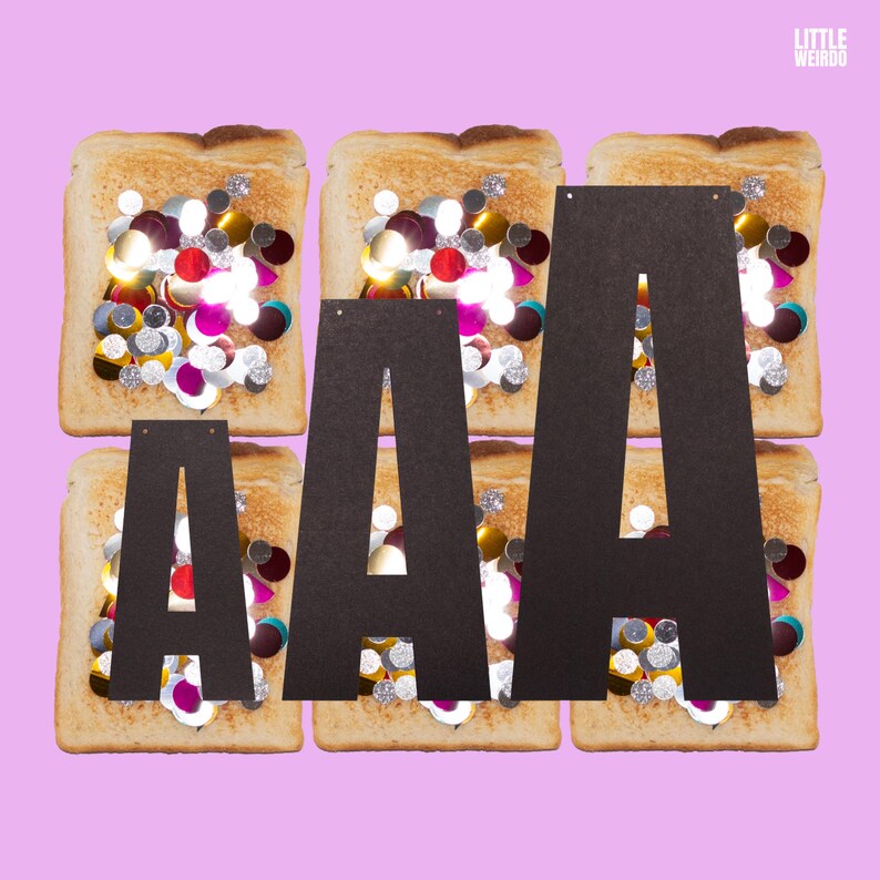 Op de afbeelding: Drie zwarte kartonnen letters die "AAA" spellen, liggen op drie toastjes die bedekt zijn met kleurrijke sprinkles. De toastjes liggen op een roze achtergrond.