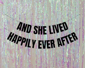 Könnte beinhalten: Schwarz-weißes Banner mit dem Text "And she lived happily ever after". Das Banner hängt vor einem schimmernden, regenbogenfarbenen Hintergrund.