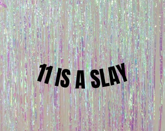 May include: A white background with iridescent, shimmering, vertical strips of plastic. The text "11 is a slay" is printed in black bold letters.