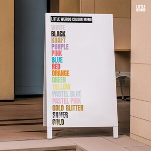 Op de afbeelding: Een wit bord met de tekst "LITTLE WEIRDO COLOUR MENU" en een lijst met kleuren in verschillende gekleurde tekst, waaronder wit, zwart, kraft, paars, roze, blauw, rood, oranje, groen, geel, pastelblauw, pastelroze, gouden glitter, zilver en goud.
