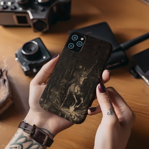May include: A black phone case with a dark, detailed image of a unicorn running through a forest. The unicorn is white with a gold horn and is surrounded by trees and a moon.