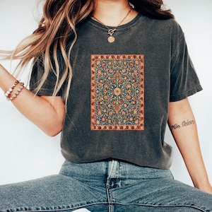 May include: A dark gray t-shirt with a vintage-style floral pattern printed on the front. The pattern is reminiscent of a Persian rug.