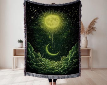 Peut inclure: Une couverture tissée avec un motif céleste. L'œuvre d'art représente un soleil jaune brillant, un croissant de lune et un ciel étoilé au-dessus de formations nuageuses vertes. La couverture a un fond noir et une bordure à franges.