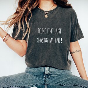 Puede incluir: Una camiseta gris oscuro con el texto "Feline fine, just chasing my tail!" impreso en blanco.