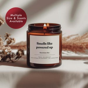 May include: A brown glass candle jar with a white label that reads "Smells like powered up Electrician Alex" and "VEGAN | ECO-FRIENDLY 100% NATURAL SOY WAX BLEND | 100% COTTON WICK".