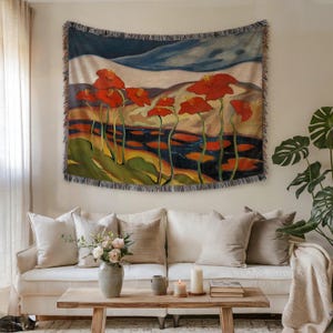 Puede incluir: Un tapiz tejido con un paisaje floral con grandes amapolas rojas. La obra de arte representa una escena estilizada con un cielo azul, una masa de agua y campos coloridos. El tapiz es rectangular con un borde con flecos, adecuado para la decoración de paredes.
