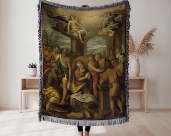 Op de afbeelding: Geweven sprei met een schilderij in renaissancestijl van een religieuze scène met figuren in gewaden, engelen en een baby. Het kunstwerk heeft een warm kleurenpalet met blauw, geel en bruin. De deken heeft een gefranjerde rand.