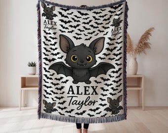 May include: A woven throw blanket featuring a repeating pattern of black bats on a white background. The blanket has a large cartoon bat in the center with the name "ALEX Taylor" printed below. Additional small bats and the name are printed on the blanket.