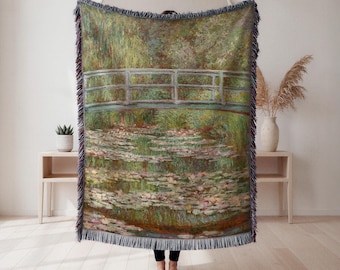 May include: Woven throw blanket depicting a famous impressionist painting of a Japanese bridge over a pond with water lilies. The artwork is in shades of green, blue, and pink, with a fringed edge.