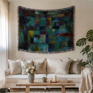 May include: A large, rectangular tapestry with a colorful abstract design in shades of teal, blue, green, and brown hangs above a white sofa. The tapestry has a fringed edge. The room is decorated with a wooden coffee table, flowers, and a potted plant.