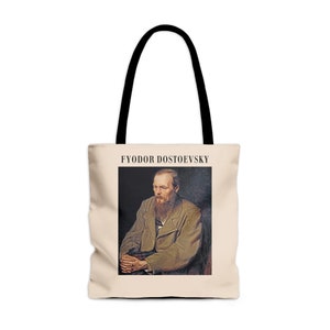 May include: A beige tote bag with black handles. The bag features a portrait of Fyodor Dostoevsky, a Russian novelist, in a brown coat and a beard. The text "FYODOR DOSTOEVSKY" is printed in black above the portrait.