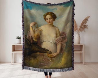 Puede incluir: Manta tejida que presenta una pintura clásica de una mujer vertiendo líquido de una jarra dorada en un cáliz dorado sostenido por un gran pájaro negro. La obra de arte tiene una paleta de colores suaves con tonos azules, rosas y dorados. La manta tiene un borde con flecos.