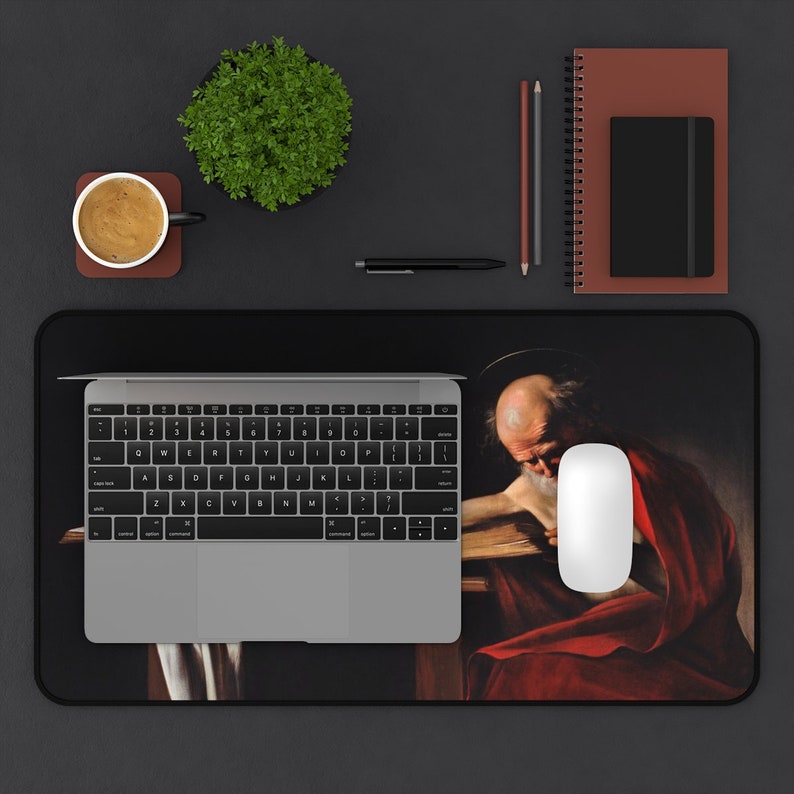 May include: A black and white mousepad with a painting of a man with a beard and a halo, wearing a red robe. The man is sitting at a table with a book in front of him.