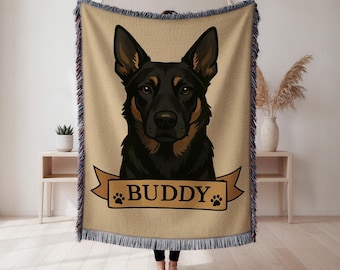 Può includere: Una coperta beige con un ritratto di cane nero e marrone e il nome "BUDDY" su uno striscione. La coperta ha un bordo con frange ed è esposta in interni.