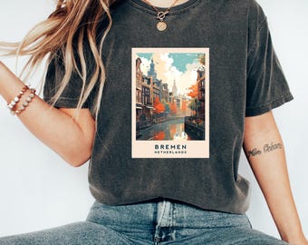 May include: A dark gray t-shirt with a vintage-style graphic of a canal scene in Bremen, Netherlands. The graphic features buildings, trees, and a body of water. The text "BREMEN NETHERLANDS" is printed below the graphic.