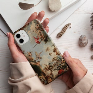 Puede incluir: Una funda de tel&eacute;fono blanca con una pintura colorida de &aacute;ngeles y una bandera roja. La funda tiene un recorte para el objetivo de la c&aacute;mara.