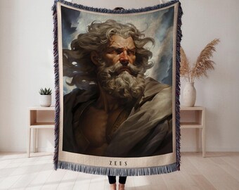 May include: Woven throw blanket featuring a portrait of Zeus with a long white beard and flowing hair. The image is framed with a blue and beige border and the name "ZEUS" is printed at the bottom. The blanket has a fringed edge.
