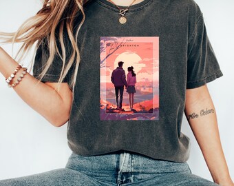 Könnte beinhalten: Ein dunkelgraues T-Shirt mit einem Grafikdruck eines Paares, das auf einem Hügel steht und auf eine Stadtlandschaft blickt. Die Grafik hat einen Sonnenuntergangs-Hintergrund und den Text "Brighton" in Weiß.