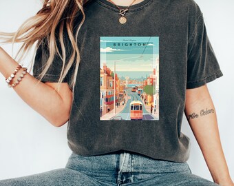Könnte beinhalten: Ein dunkelgraues T-Shirt mit einer Grafik im Vintage-Stil, die eine Straßenszene in Brighton, England, zeigt. Die Grafik zeigt eine rote Straßenbahn, Gebäude und den Text "Brighton".