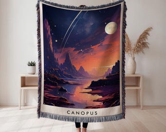 Peut inclure: Une couverture tissée avec un paysage céleste. L'image montre un ciel nocturne avec une lune, des étoiles et une étoile filante au-dessus d'une chaîne de montagnes et d'un lac. Le mot "CANOPUS" est affiché en bas.