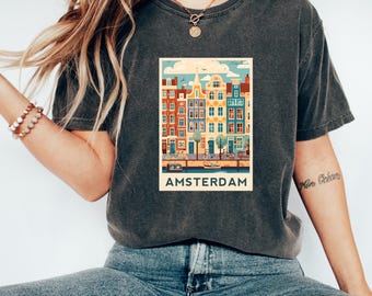 May include: A dark gray t-shirt with a vintage-style illustration of Amsterdam's canals and buildings. The illustration is in a retro color palette and includes the text "AMSTERDAM".