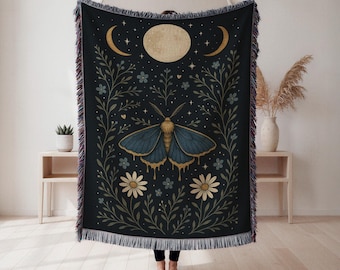 May include: A dark blue throw blanket featuring a moth with blue wings and gold accents, surrounded by floral and celestial designs. The blanket has a fringed edge and measures approximately 60 inches by 50 inches.