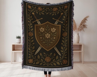 Op de afbeelding: Een zwarte sprei met een schild, gekruiste zwaarden en bloemmotieven. Het schild is bruin met een bloemmotief, omgeven door rozen en bladeren in goud en beige. De sprei heeft een gefranjerde rand.