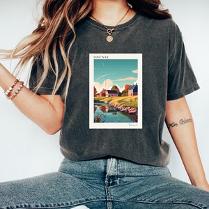 May include: A dark gray t-shirt with a graphic print of a colorful illustration of a town with the text "ODENSE" and "Denmark" printed below the image.