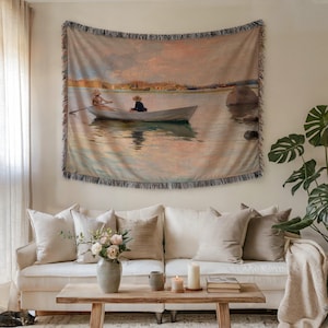 May include: Woven tapestry wall hanging depicting a tranquil waterscape with a boat. The artwork shows two people in a rowing boat, with a soft colour scheme of blues, pinks, and beige. The tapestry has a fringed edge.