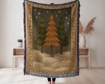 Könnte beinhalten: Eine gewebte Wurkdecke mit einer Winterwaldszene mit drei Bäumen in Grün- und Orangetönen vor einem dunkelgrauen Himmel mit Sternen. Die Decke hat einen dekorativen Rand und Fransen.