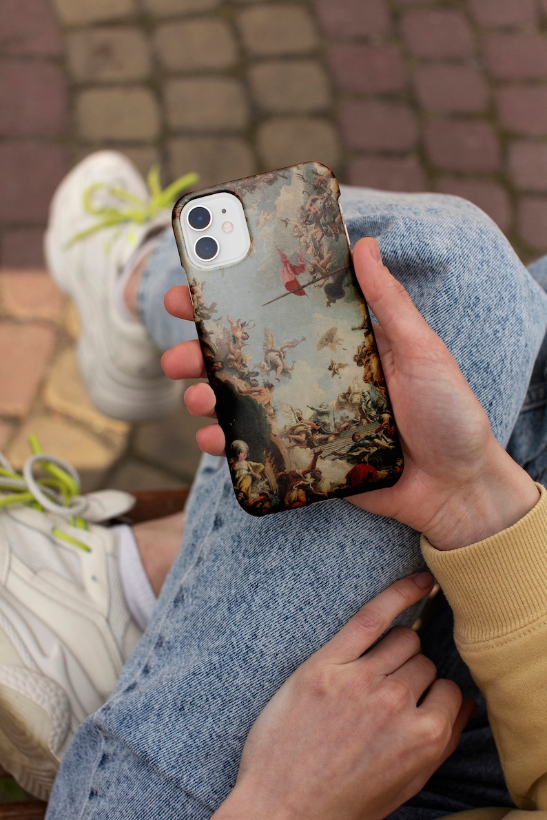 Puede incluir: Una funda de tel&eacute;fono blanca con una pintura colorida de estilo renacentista de &aacute;ngeles y figuras. La funda tiene una protuberancia de c&aacute;mara elevada con tres lentes.