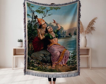 Könnte beinhalten: Eine gewebte Decke mit einer lebendigen Illustration von zwei Figuren in traditioneller indischer Kleidung. Das Kunstwerk zeigt eine ruhige Szene mit einem See, Bäumen und einem sanften blauen Himmel. Die Decke hat einen Fransenrand und wird vor einem neutralen Hintergrund präsentiert.