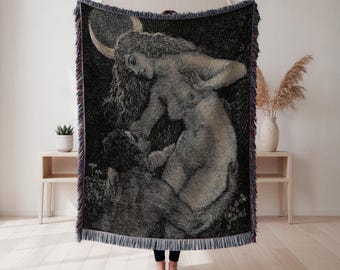 May include: Black and white woven throw blanket featuring an illustration of a woman and a man. The woman has long curly hair and a crescent moon above her head. The blanket has a fringed edge with purple and blue accents. The blanket is displayed in a room with light-colored wood floors.