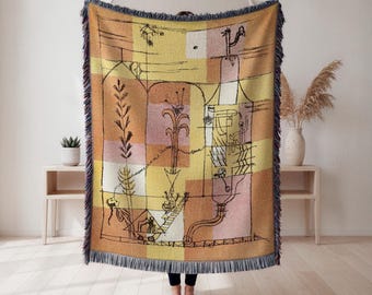 May include: A woven throw blanket with a geometric design in shades of yellow, orange, and pink. The blanket features black line art depicting abstract figures and shapes. The edges are finished with a fringe.